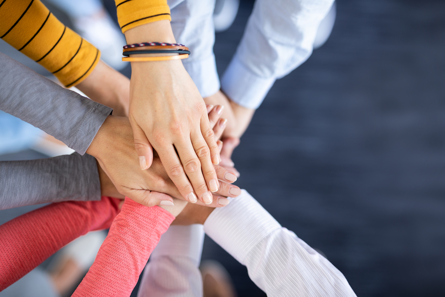 Inquadratura ravvicinata dall'alto di un team che unisce le mani al centro per dimostrare solidarietà, unione e lavoro di squadra.