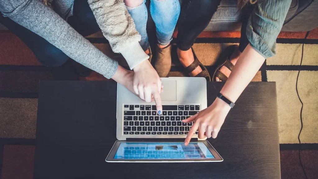 Tre persone riunite attorno a un laptop, indicano lo schermo mentre navigano online insieme.