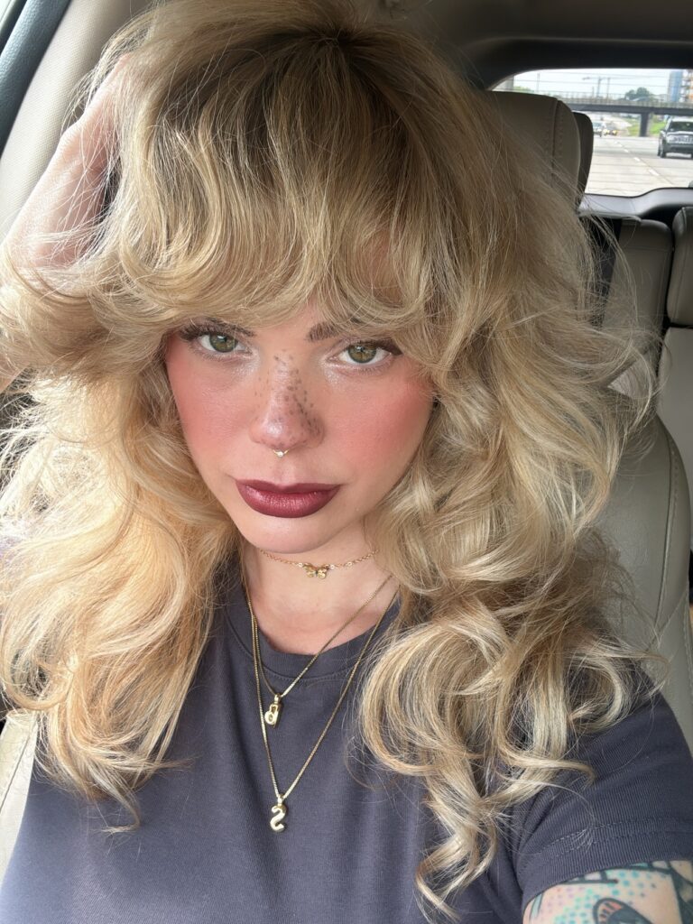 A woman with voluminous blonde curly bangs cut longer to account for shrinkage and highlight natural texture.