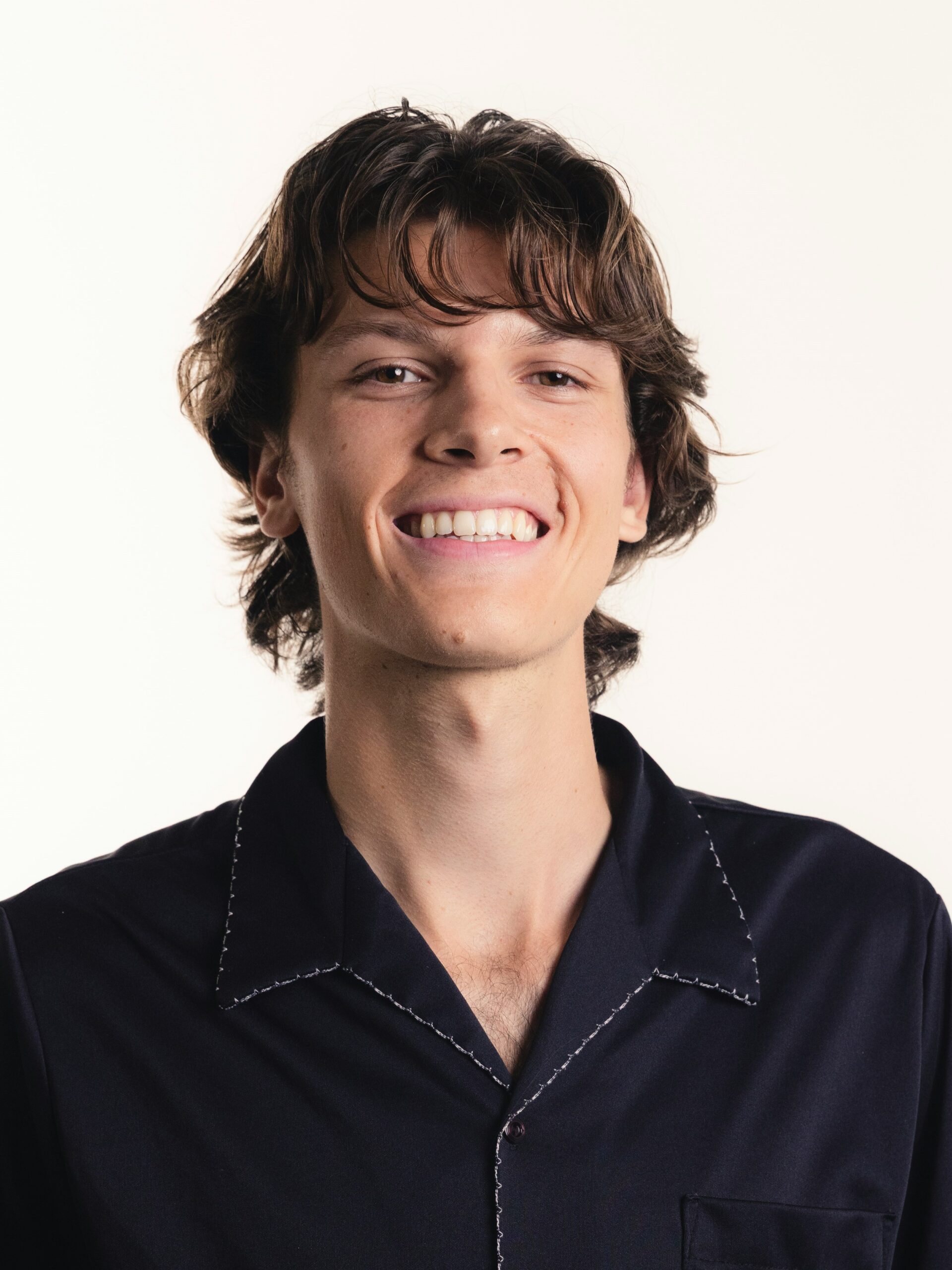 Un giovane uomo con un mullet scalato e con movimento, camicia blu scuro, sorridente.