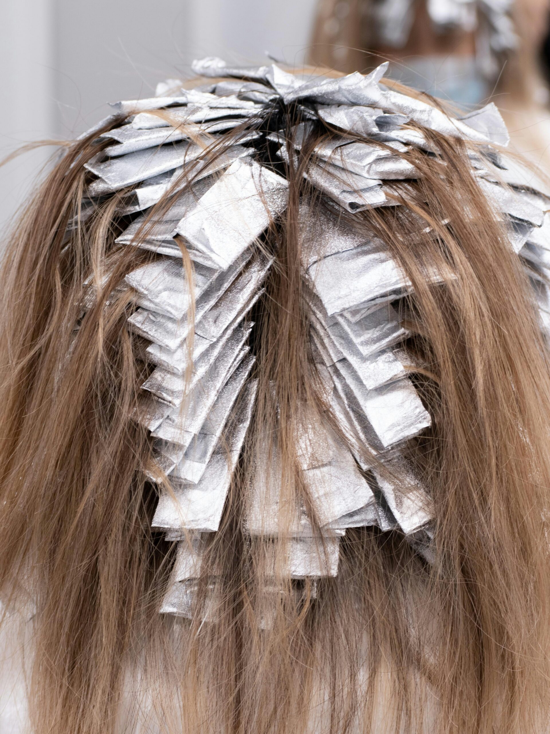 Nuca di una cliente con le cartine nei capelli durante un trattamento di colorazione parziale dal parrucchiere