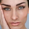 Primo piano del viso di una donna con microblading sulle sopracciglia, trucco naturale e capelli scuri raccolti