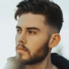 Uomo in piedi all'aperto con capelli scuri e un taglio taper fade con la parte superiore strutturata