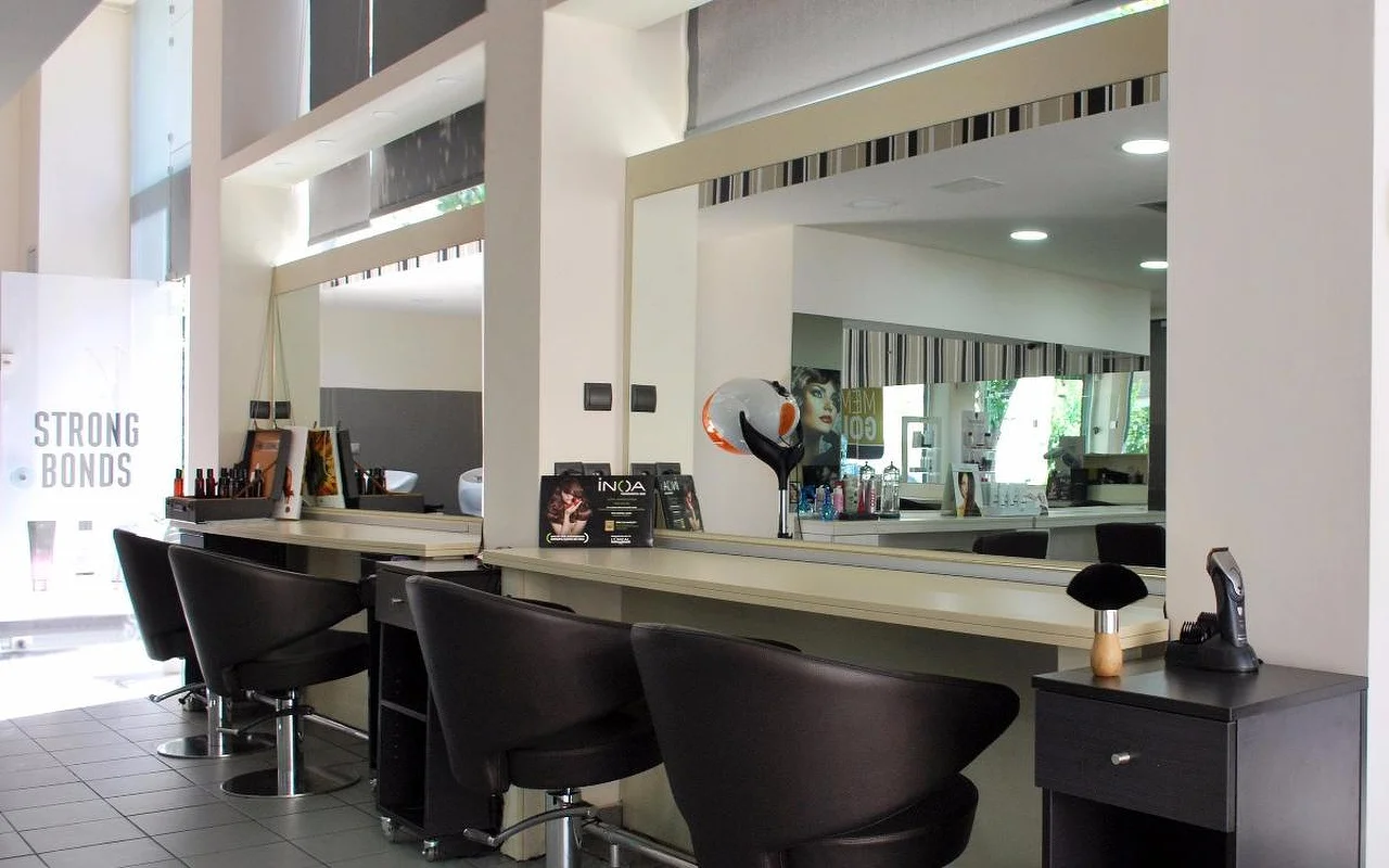 Un salone di parrucchiere professionale con poltrone scure in pelle per lo styling di fronte a grandi specchi, prodotti per capelli allineati lungo il bancone, soffitti alti e luce naturale che filtra attraverso le vetrate a sopraluce.