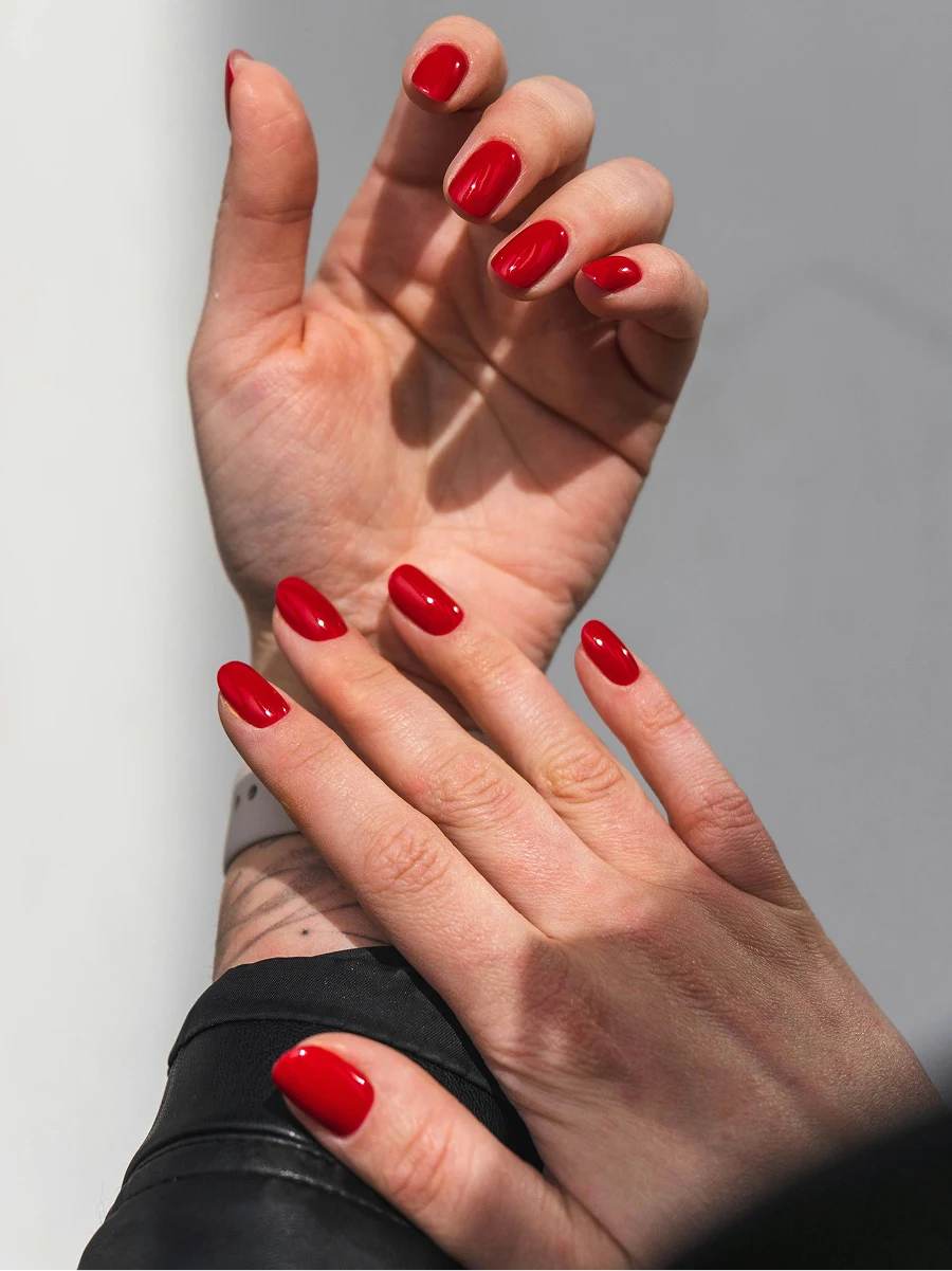 Primo piano degli avambracci di una donna con giacca di pelle nera, che mostrano una manicure in gel rossa e lucida