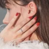 Vista laterale ravvicinata della testa di una donna castana, con la mano appoggiata al viso che mostra una manicure in gel rossa e lucida