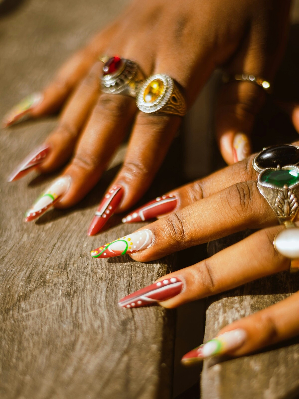 Primo piano delle mani di una donna con unghie acriliche a stiletto rosse e bianche, decorate con pois e volute gialli e verdi