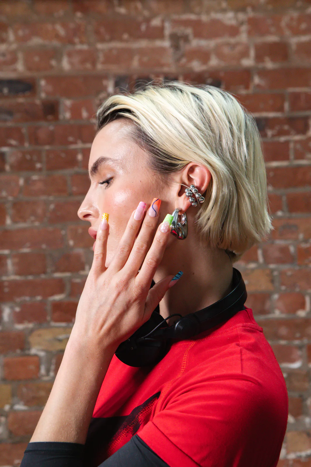 La DJ e attrice Rex Adams di profilo, con le cuffie al collo, mentre mostra i french tip al neon della colorata electric mani