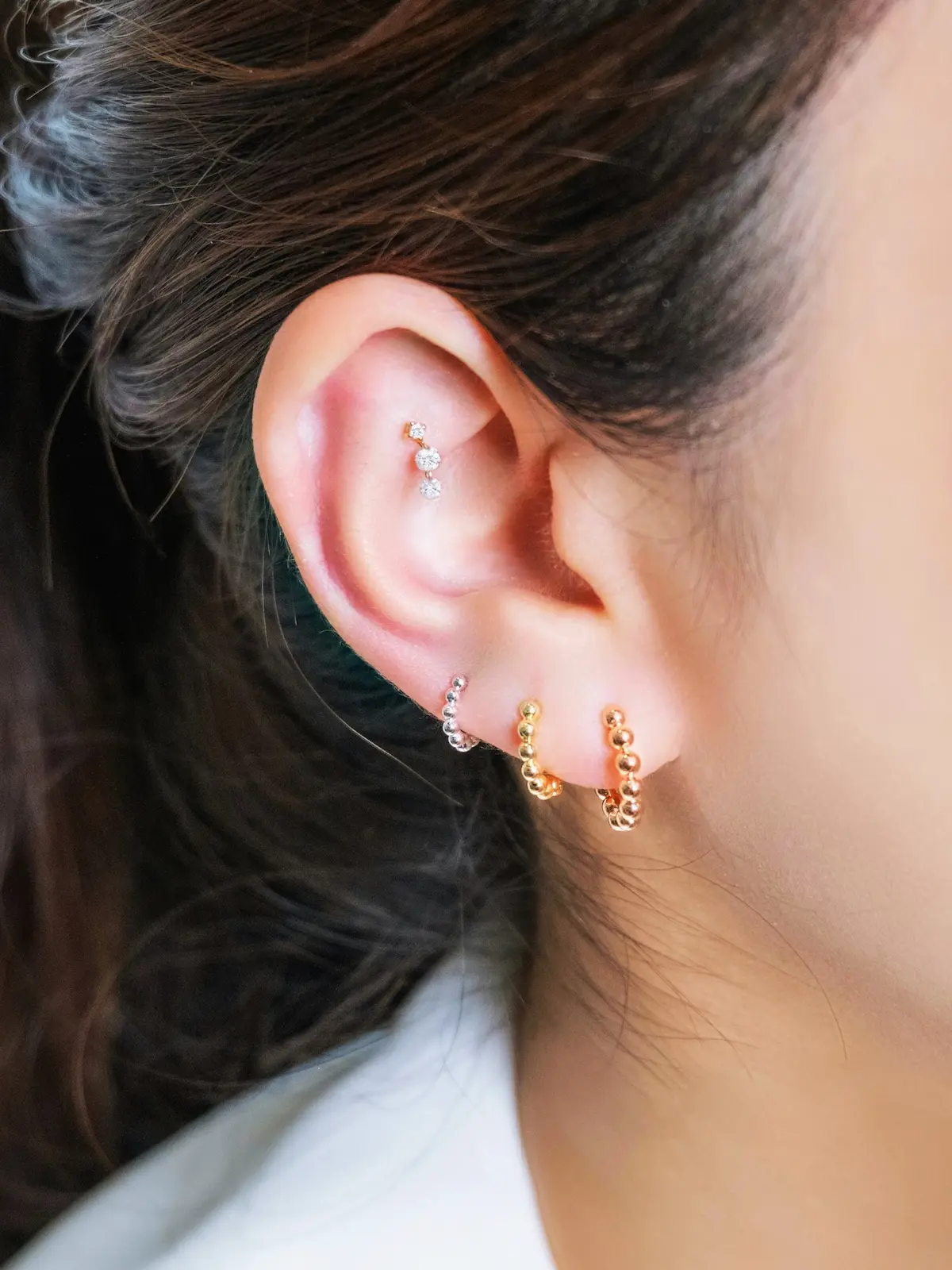 Primo piano dell’orecchio di una donna con vari cerchietti e un punto luce all’helix