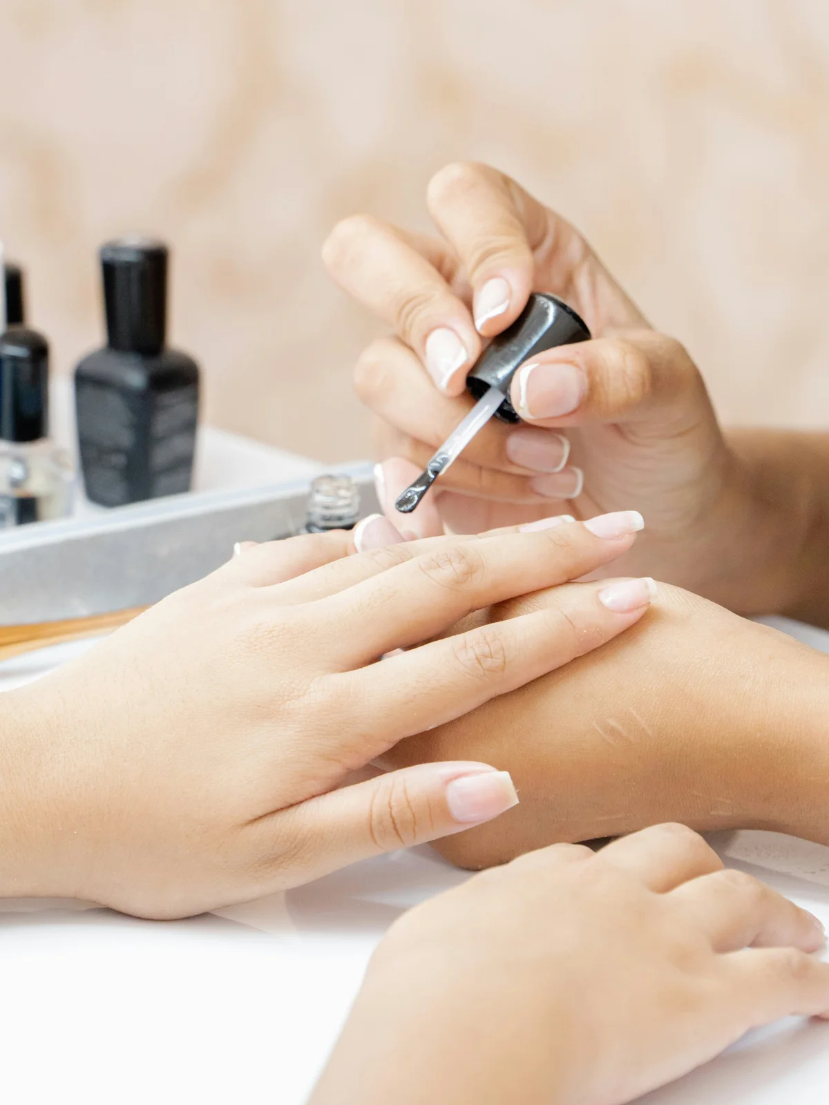Primo piano di una manicurista che applica un trattamento rinforzante trasparente sulle unghie di una cliente in salone