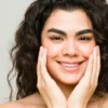 Una giovane donna dalla pelle pulita e dai capelli scuri e mossi sorride verso l'obiettivo