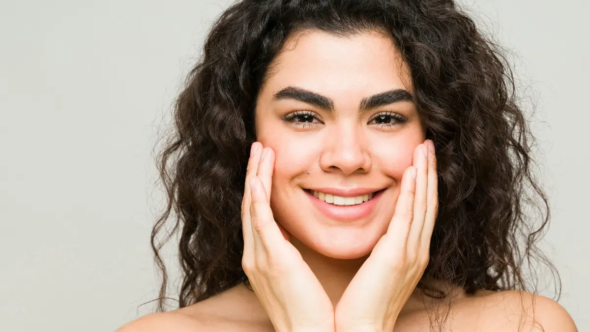 Una giovane donna dalla pelle pulita e dai capelli scuri e mossi sorride verso l'obiettivo