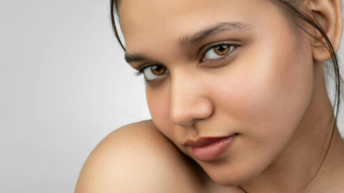 Primo piano di una donna che sorride alla fotocamera con una pelle liscia e senza trucco