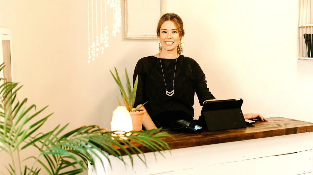 Una donna sorridente dietro il bancone della reception di un centro estetico