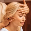 Primo piano di una donna con gli occhi chiusi mentre una professionista, durante un massaggio indiano della testa, le appoggia una mano sulla fronte e con l'altra le massaggia il collo