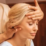Primo piano di una donna con gli occhi chiusi mentre una professionista, durante un massaggio indiano della testa, le appoggia una mano sulla fronte e con l'altra le massaggia il collo