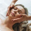 Donna rilassata durante un trattamento di linfodrenaggio al viso, mentre il professionista esegue delicati movimenti sulle guance