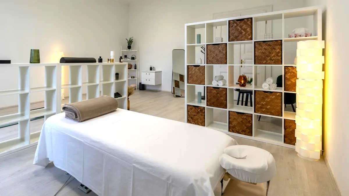 Cabina di un centro estetico pulita e ordinata, con il lettino preparato con lenzuola e una coperta arrotolata, pronta per un massaggio